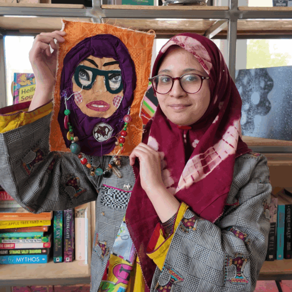 Atiyya Mirza holding a fabric self-portrait next to her head.