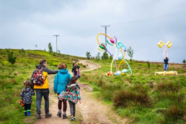A family explore the outdoors Wild Uplands sculpture trail with colourful artwork in the background.