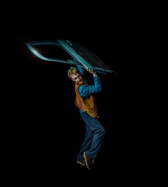 Boy holding a car door above his head, stood in a poised position.