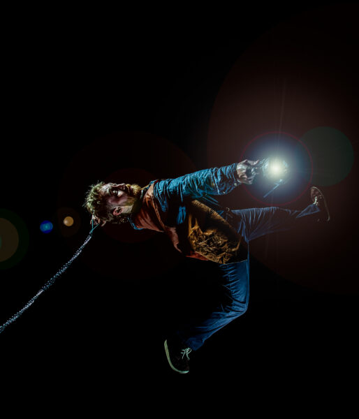 Boy leaning backwards with arms stretched out. Holding a torch in one hand.
