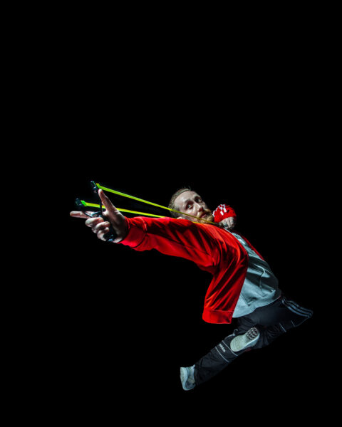 Male jumping in the air wearing a red jacket with a green slingshot.