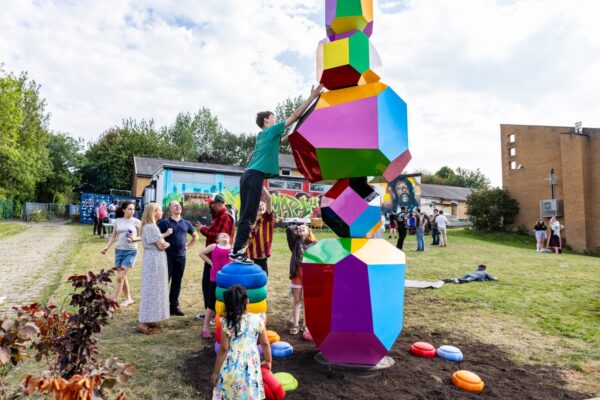 Young people interacting with the colourful obelisk-shaped structure.
