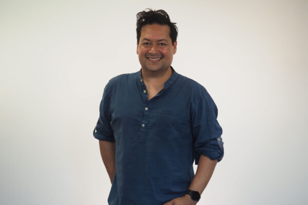 Nick Ahad stands in a blue shirt, smiling towards the camera.