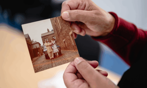 A pair of hands holds a photograph - women wearing South Asian dress pose in front of a car.