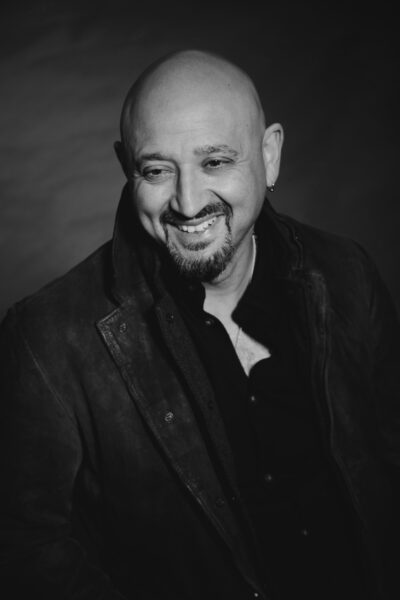 A black and white photo - a man poses for the camera, he is wearing a black shirt.