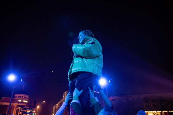 A woman is lifted into the night air, wearing a puffy jacket.
