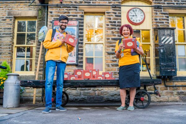 Two smiling Bradford 2025 volunteers holding a red box.
