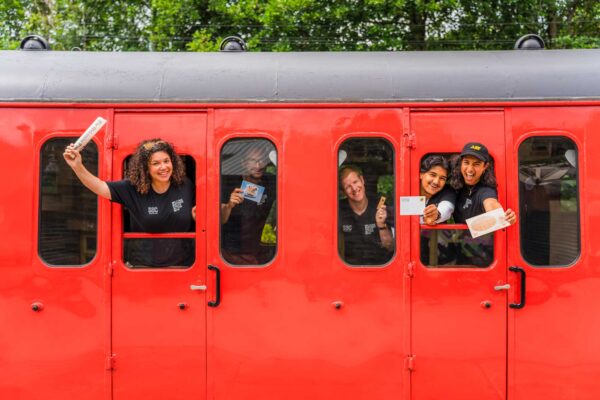 Smiling people inside a red train carriage, looking out of the windows.