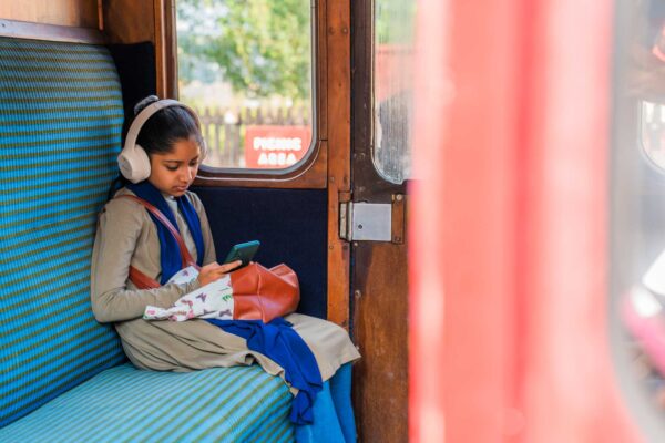 A young girl sitting in an old fashion train carriage wearing headphones.