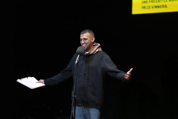 A man talks to the crowd, his arms opened wide.
