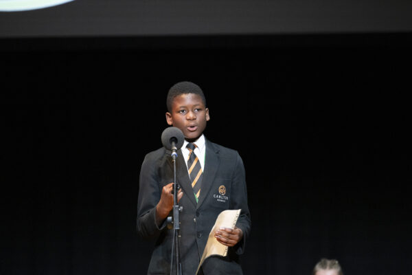 A young boy performs into the microphone - he is wearing a green blazer.