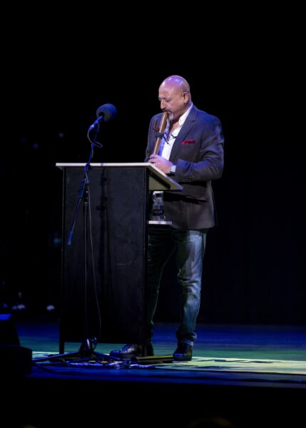 A man in a suit stood playing a wind instrument on stage