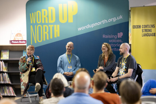 Four people sit on a stage - the woman on the left is speaking into a microphone.