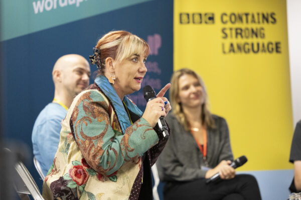 A woman with white and red hair speaks into a microphone.