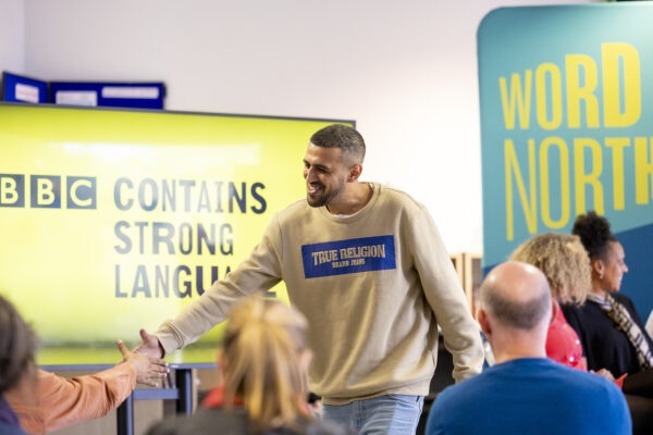 A man shakes hands with an audience member- a big smile on his face.
