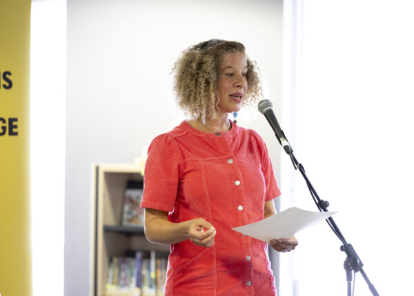 A woman with curly hair reads into a microphone.