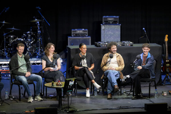 Five people sit on the stage - three men and two women.