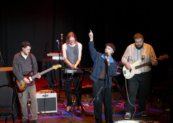 A man performs with a band - he is posing with his hand in the air.