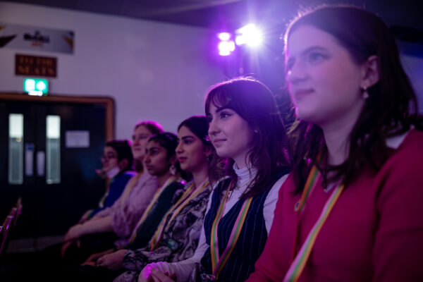 A group of young people sat in an audience laughing.