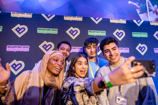 A group of five young people stood together taking a selfie in front of a Bradford 2025 sign.