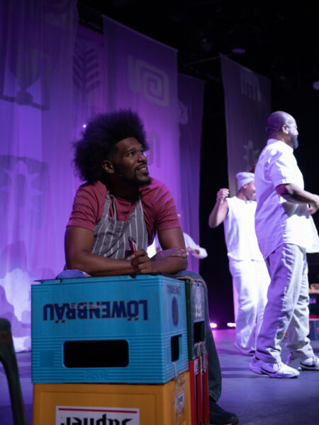 A black man with an afro leans on a stack of crates.