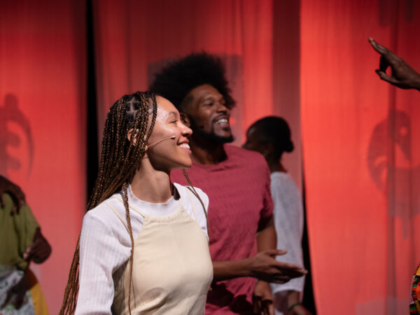 A black woman with braids smiles in the foreground, while a black man with afro smiles in the background.