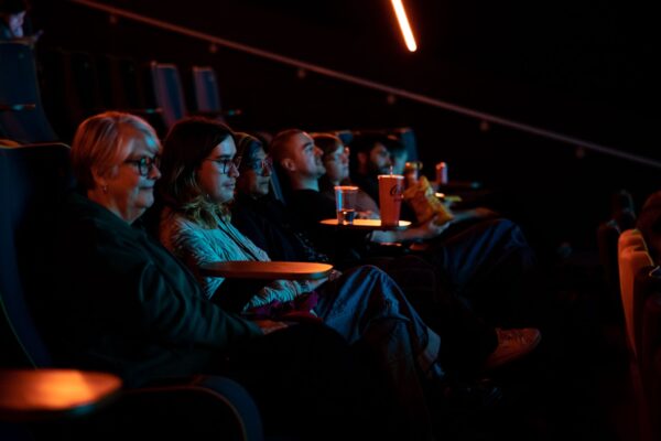 A row of people sit looking at a cinema screen.