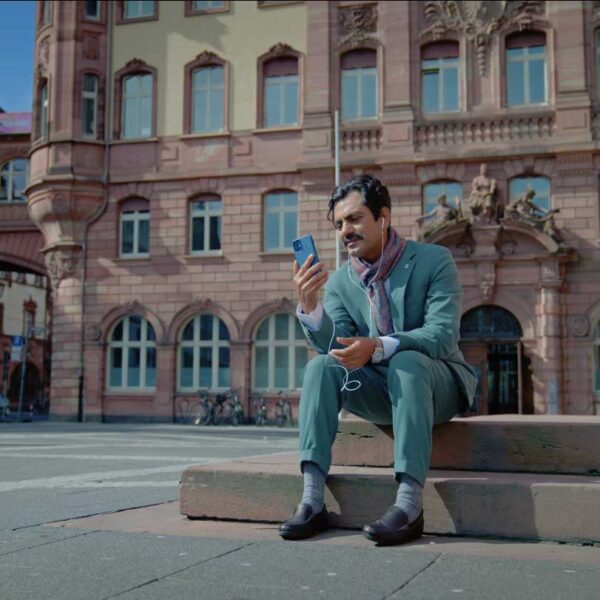A man in a turqoise suit sits on some urban steps, looking at a phone.