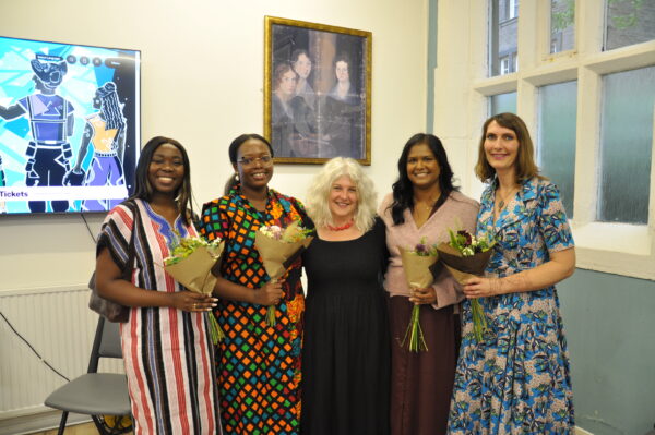 Five women pose for the camera, some of them are holding flowers.