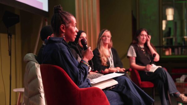 Panellists on stage. A woman closest to us holds a microphone.