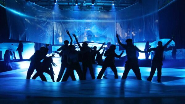 An image from a stage performance, with dancers in silhouette lit in blue light.