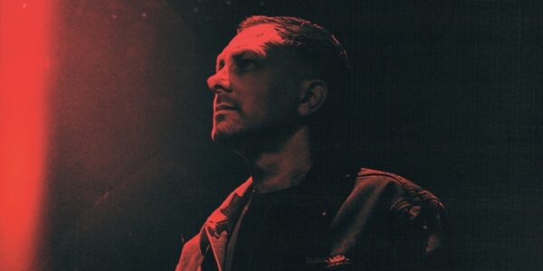 A red and black image of a man with short dark hair looking away from the camera.