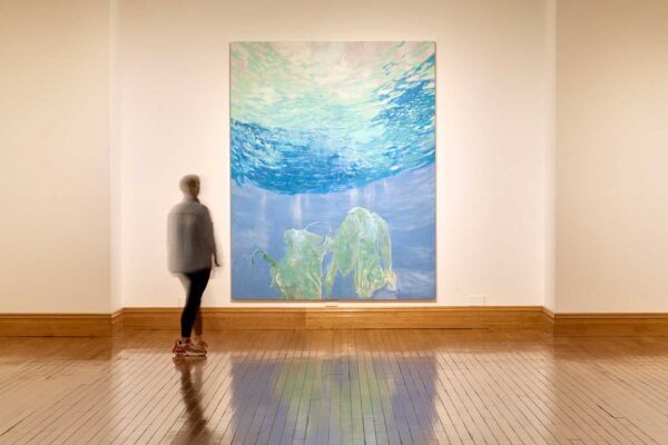 A person stands in front of a large blue and white painting, on a white wall.