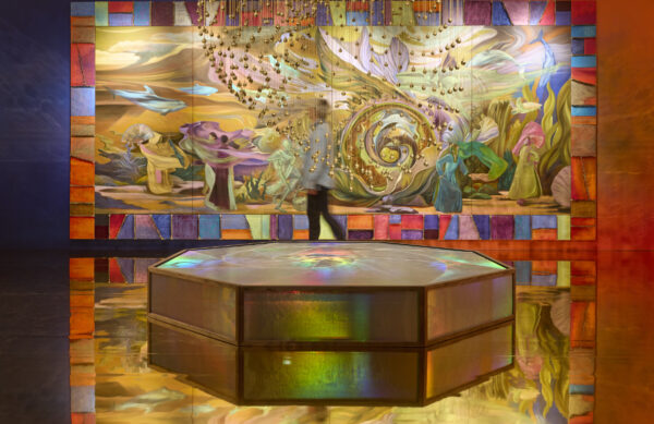 A painting on a wall in front of us, with a swirled sculpture hanging down from the ceiling in between us and the painting. There is a large 6 sided object in the centre of the room.