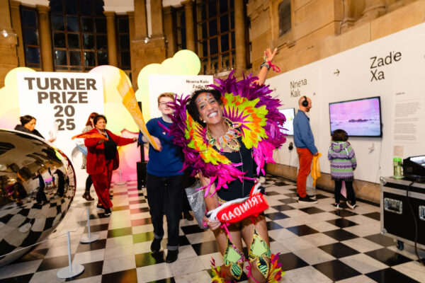 A lady dancing and smiling wearing bright colourful feathers
