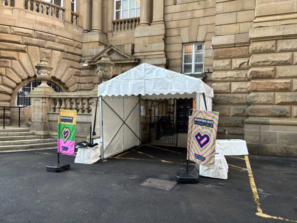 A white gazebo tent with two Bradford 2025 flags. This is the accessible entrance to Cartwright Hall for the Turner Prize 2025.