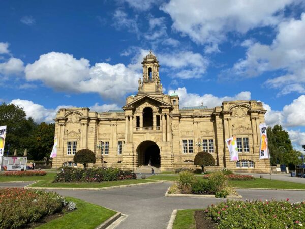 The exterior of Cartwright Hall Art Gallery, a grand building in Bradford's signature yellow gold sandstone. There are several flags outside, with the Turner Prize 2025 branding on them.