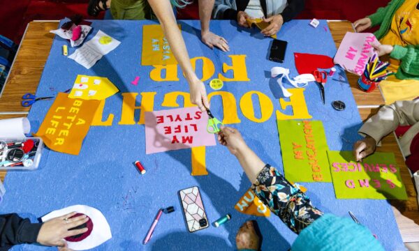 Looking down on a colourful banner made of felt, there are pairs of scissors, hands and pieces being worked on.