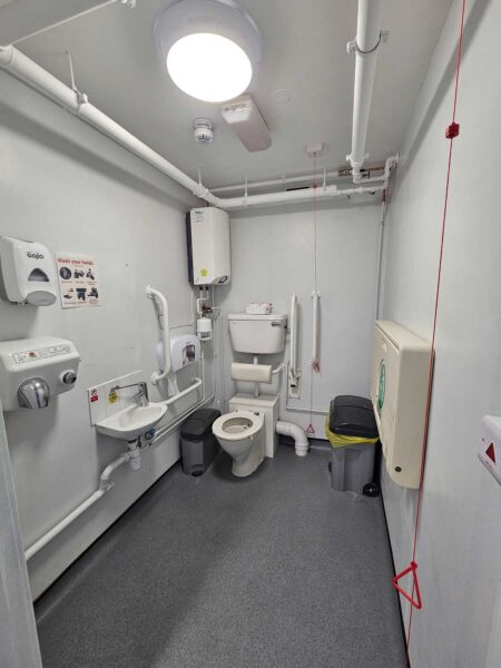 The interior of the accessible toilet at the TFD Centre, with red emergency cord, toilet, basin, handles and baby changing table