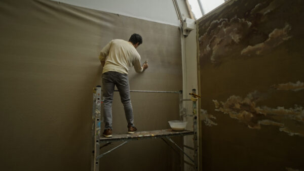 Artist Mohammed Sami works on a canvas. We only see the back of his body, wearing a white shirt.