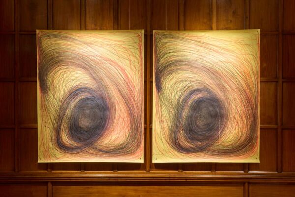 Two drawings side by side hanging on the wall of a gallery. The drawings are almost a mirror of each other, showing swirled round patterns, created rhythmically by the artist Nnena Kalu.
