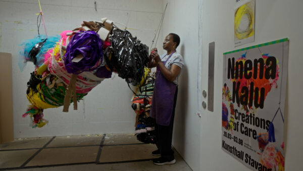 Artist Nnena Kalu in her studio. She stands wrapping tape around a colourful abstract sculpture hanging from the ceiling.
