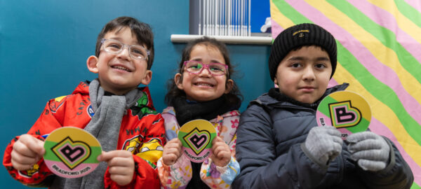 Three children smile, holding Bradford 2025 logos.