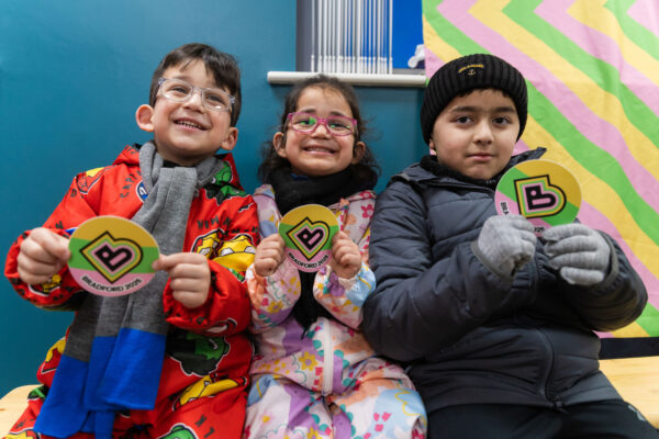Three children smile, holding Bradford 2025 logos.