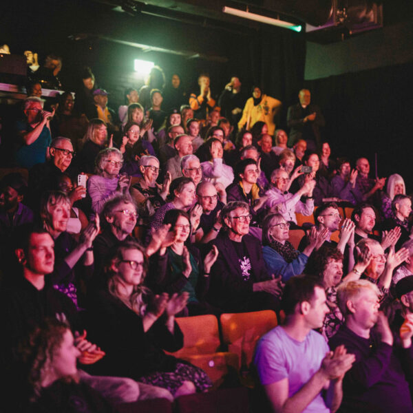 An audience in Loading Bay applaud with smiling faces.