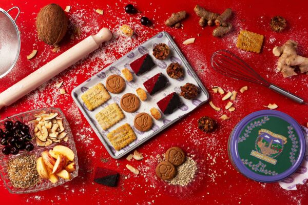 A red rable with lots of biscuits and baking items. There is a tray in the centre with colourful biscuits, a rolling pin and a biscuit tin.