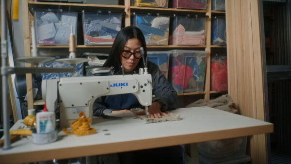 Artist Zadie Xa works at a sewing machine. She wears glasses with thick black frames.