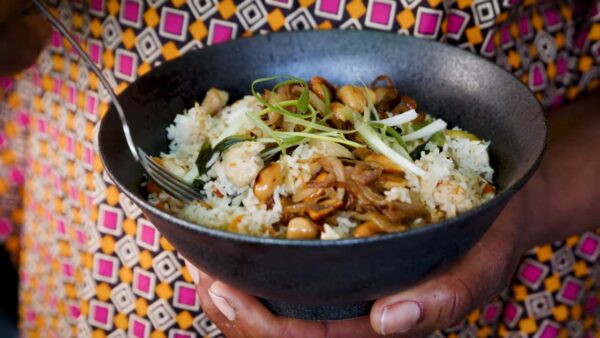 A bowl of delicious food, held in a person's hand. It contains rice and vegetables.