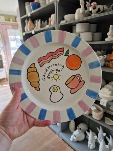 A painted plate with bacon, croissant, orange and a cup of tea