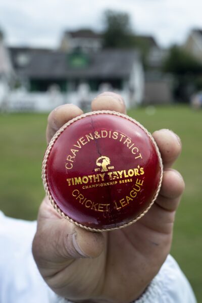 Hand holding a red cricket ball that has timothy taylors written on it.